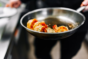 man chef cooking tasty shrimp in frying pan on kitchen
