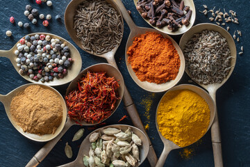Set of spices in brass spoons, closeup, top view. Various peppers, cardamom, carnation, turmeric, paprika and saffron for cooking