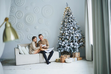 Obraz premium A happy couple celebrates the New Year at home near a Christmas tree decorated with toys and garlands. Lovers welcome the new year together. New Year and Christmas concept. February 14th.