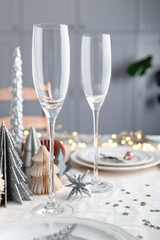 Xmas table settings in white and pink colors with trendy paper christmas trees on background, empty plates and glasses ready for festive dinner and party