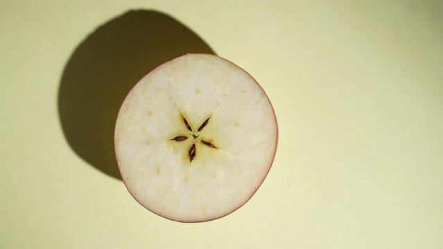Half fresh apple rotating on the sunlight on a colored yellow background, close up, top view. Food concept