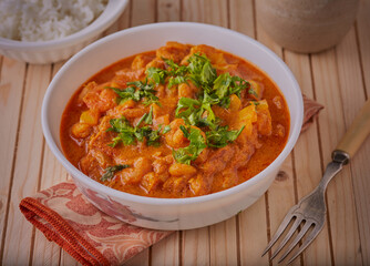 Thai styled prawn curry garnished with herbs on a wooden table.