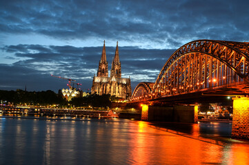 Cologne, Germany. Famous Hohenzollern Bridge over Rhine river. Buildings in historic city centre. Towers of Cathedral and city hall by night.	
