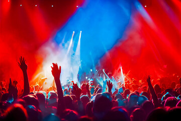 Vibrant tricolored lights under a rock concert, blue, white and red spotlights illuminating a boiling crowd. Energy, smoke and captivating colors.