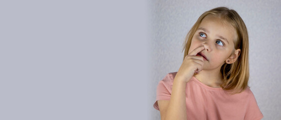 Little cute girl with blond hair picks her nose. The child clears his nose and thinks about...