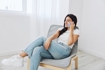 Naklejka na ściany i meble A woman talking on the phone at home sitting in a chair and smiling with her teeth, online communication as a lifestyle