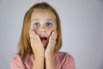 Frightened little girl looks at the camera worried about something with her hands on her face and her eyes wide open