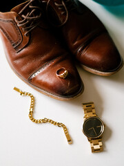 Man's accessories for wedding. Vintage brown leather shoes with golden ring and wristwatch