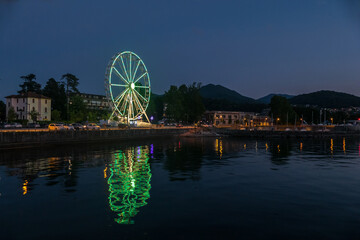 Ferris wheel illuminated in the evening with the lights reflecting on the Lake Maggiore in Luino