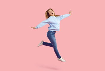 Smiling young woman having fun bouncing with arms outstretched, isolated on pastel pink background...