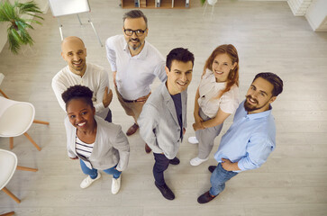 Team of happy multiracial business colleagues smiling together looking up in office. Top view of...