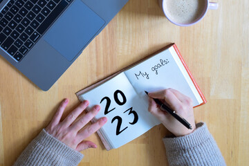 Young woman hand writing in a 2023 new year notebook with list of resolutions while drinking a...