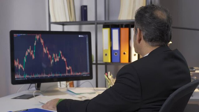 Businessman monitors stock sales statistics. Investment concept. Office. Man Using Computer with Screen Displaying Real Time Stocks, Currency Market Charts.