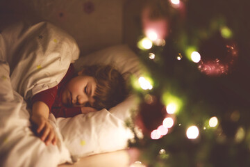 Little cute toddler girl sleeping under Christmas tree and dreaming of Santa at home, indoors....