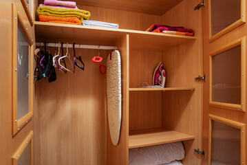 Hangers, towels, clothing iron in an open wooden wardrobe