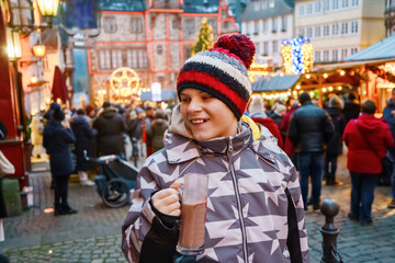 Fototapeta na wymiar Little cute kid boy drinking hot children punch or chocolate on German Christmas market. Happy child on traditional family market in Germany, Laughing boy in colorful winter clothes