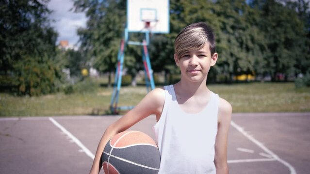 Portrait of a boy with a ball on a basketball field looking at the camera and smiling, moving camera, steadicam shot