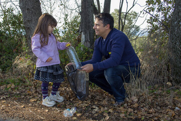 Image of a little girl with her dad who collects plastic bottles and throws them in a bag. Teaching about recycling and respect for the planet
