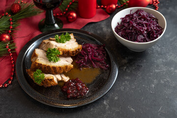 Roast pork slices with red cabbage, jam and sauce for a festive holiday dinner, napkin and Christmas decoration on a dark background, copy space, selected focus