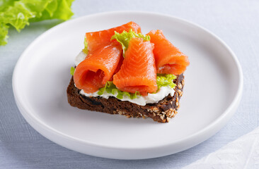 Salmon fillet sandwich with cream cheese on a light wooden table