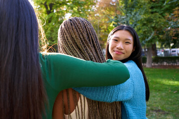 Affective photo of three female friends embracing outdoors at a public park, while one of them...