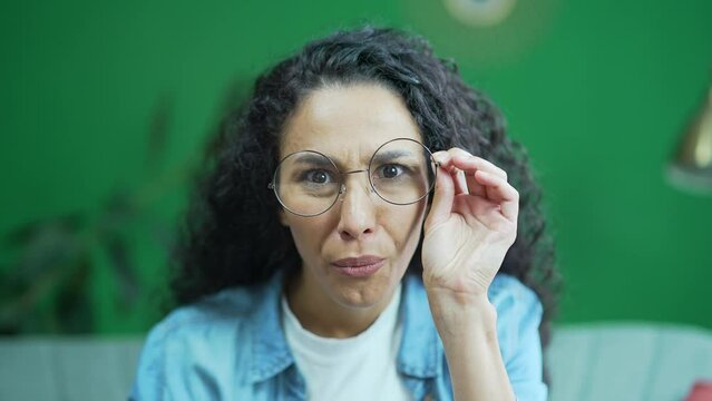 Camera view of amazed shocked young curly woman with glasses looking into camera demonstrates wow surprised face expression indoors Happy lady rejoices by sudden incredible news promotion sale at home