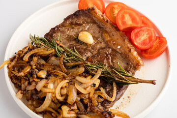 Juicy steak with fried onions and cherry tomatoes on a white plate. Close-up