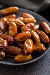 Dried dates fruit on plate on black table.