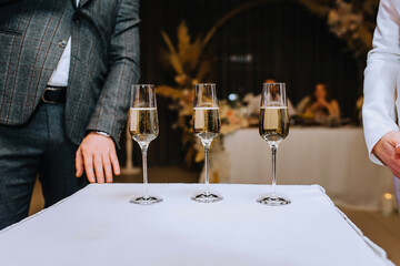 Three glass wine glasses with champagne are on the table at the wedding. Photography, competition.