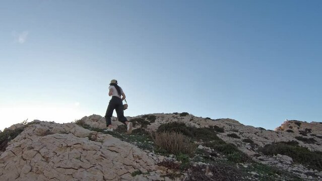 A young Caucasian girl climbs with a left-handed run up the very peak of a mountain in the afternoon on the island of Friulle in France, a side view with slow motion and tracking to the left. Journey 