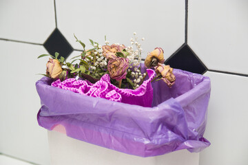 Waste bin full of old discarded flowers. Flowers in the trash, bouquet in the urn, discarded bouquet