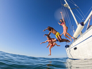 Group of friends diving in the water during a sailboat excursion, young people jumping inside ocean...