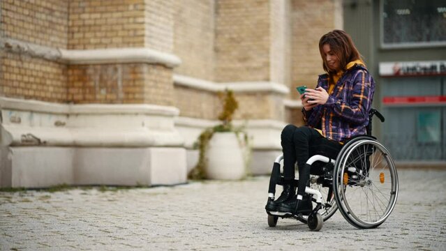  Woman with disability who uses a wheelchair using a smartphone in the city