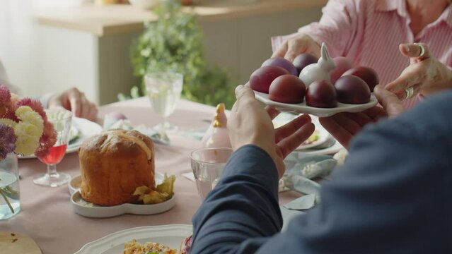 Family passing plate of dyed eggs to father and little daughter while having festive dinner on Easter day