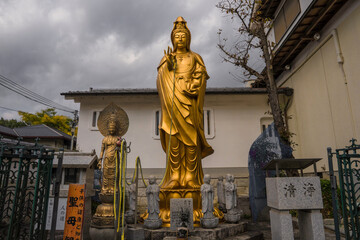 This image shows a gold statue in front of Japan shrine with a moody sky in the background. - Powered by Adobe