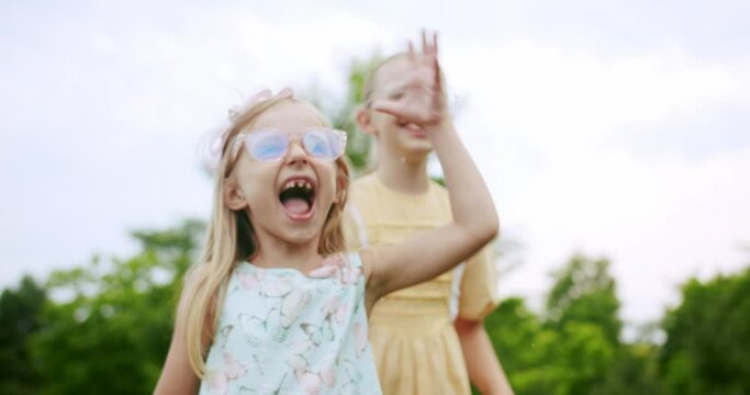 Laughing girls catching soap bubbles in park. Amazed preteen girls in dresses and glasses having fun in summer garden and catching shiny flying soap bubbles and laughing