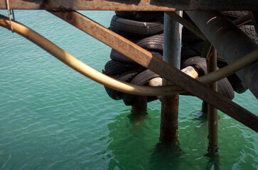Naklejka premium Pier detail with stacked rubber wheel tires hanging on piles above sea water