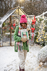 Portrait of a young woman holding magazine with New Year's cover at snowy backyard decorated for a winter holidays