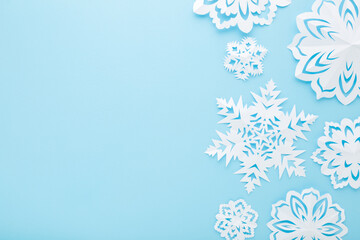 Different white snowflake shapes created from paper on light blue table background. Pastel color. Closeup. Top down view. Handmade decoration elements for winter festive. Empty place for text.