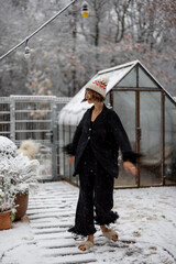Young woman in sleepwear and hat dancing at snowy backyard, enjoying morning time outdoors on winter time. Good morning and happy winter time concept