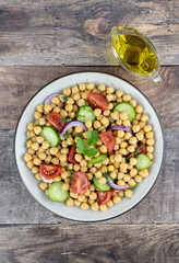 Chickpea salad with tomatoes, cucumbers, onions and olive oil on a wooden background. Top view. Selective focus. Oriental and Mediterranean cuisine. 