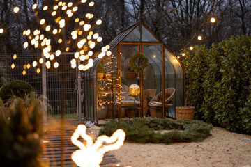 Beautiful backyard with vintage glasshouse and Christmas wreath decorated with garlands during...