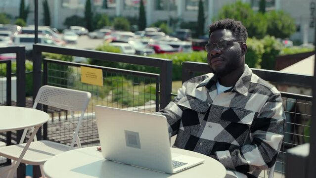 smart black man is working with laptop computer on open terrace of street cafe in summer day