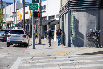 a man and a woman with long braids walking along a sidewalk in Hollywood with shops and parked cars...