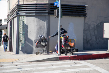 a homeless man wearing a black hoodie with two metal shopping carts on the corner of Yucca Street ...
