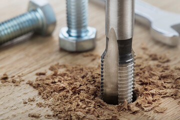 Thread tap drill cutting hole in wooden plate. Working cutter.