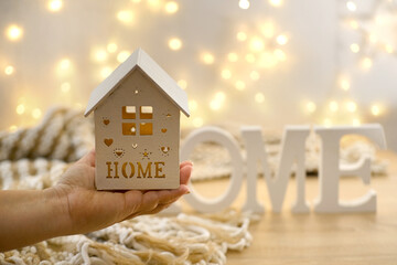 wooden house with candle on female hand, beautiful blurred background, cozy creamy plaid with...