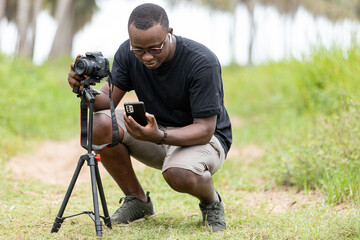 Portrait of an African photographer taking a picture with a digital camera while setting up his...
