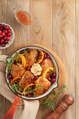 Baked chicken thighs with orange, cranberry and spicy herbs rosemary servered in frying pan on light wooden rustic background. Festive Christmas Dinner Concept menu. Top view. copy space