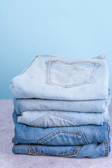 Stack of jeans pants on blue background. Fast fashion concept